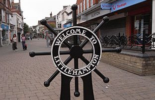 Black decorative sign with "Welcome to Littlehampton" in white, located on a pedestrian street.