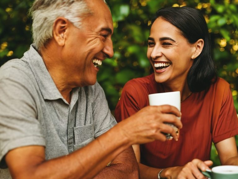 A client and care giver laughing together, enjoying drinks in a lush green setting.