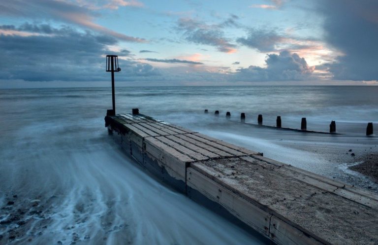 Wooden Groyne in Goring extending into a turbulent sea under a cloudy sky at twilight.